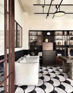 Modern living room with white couch, black and white patterned rug, and black bookshelf with various decorative items.