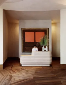 Modern lobby with a ribbed concrete reception desk, abstract painting, and wooden floor.