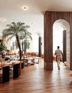 Modern restaurant interior with wooden walls and furniture, plants, and contemporary decor.