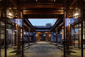 A beautifully designed lobby with wooden beams, glass windows, and stone flooring, illuminated by warm lighting.