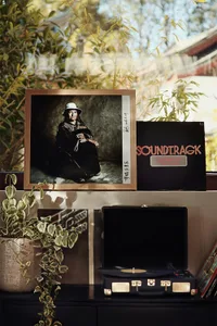 A record player sits on a shelf by a window surrounded by plants.