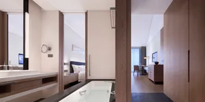 Modern residential bathroom featuring wood finishes and marble accents, with a view into the adjacent room.