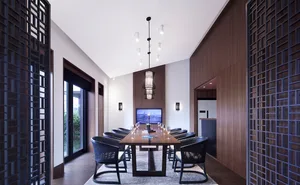 A minimalist conference room with a long wooden table, black chairs, and a large window on one side.