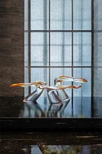 A modern glass sculpture displayed in an interior setting with a large window.