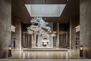 A modern hotel lobby featuring a large, metallic tree sculpture on a stone pedestal with tall columns and a skylight.