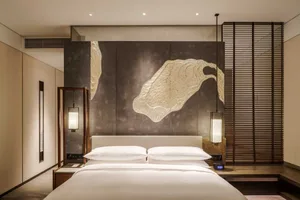 Modern bedroom with soft furnishings including a white blanket on the bed, a hanging lamp, and a decorative wall panel.