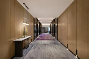 A modern corridor with wood-paneled walls and marble flooring, illuminated by hanging glass pendant lights.
