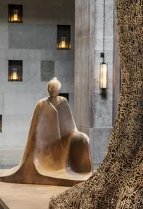 A metal statue of a seated figure in a lobby setting.