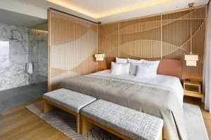 A modern minimalist bedroom featuring a wooden panel wall with geometric patterns, a glass-enclosed shower area, and marble f