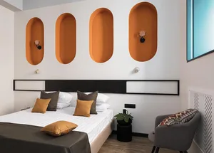 A minimalist bedroom featuring a large bed with white bedding, brown and orange decorative pillows, and orange wall niches.
