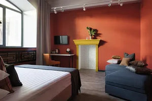 Modern minimalist bedroom featuring a bed with a wooden frame and fabric bedding, accompanied by a concrete fireplace and a b