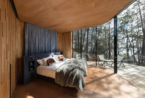 Modern minimalist bedroom featuring wood paneling, a comfortable bed, and a view of a natural outdoor setting.