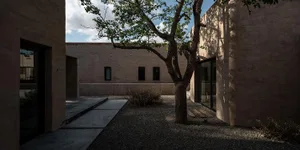 Modern garden featuring concrete walls, gravel pathway, and glass doors with a tree and vegetation