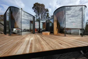 A modern residential structure featuring large glass windows and wooden flooring.