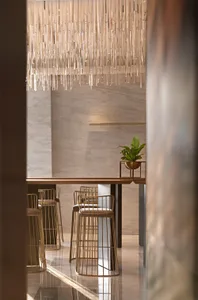 Modern restaurant interior with glass chandelier, wooden table, and brass stools.