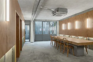 Industrial-style meeting room with concrete walls and floor, long wooden table with chairs, and a large window.