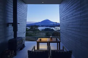 Modern minimalist living room with a view of a mountain landscape, featuring a wooden table, chairs, and a fireplace.