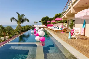 A minimalistic swimming pool deck with lounge chairs, umbrellas, and large balloons in the pool.