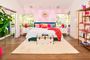 Modern bedroom featuring a white bed with pink and blue accents, surrounded by white furniture and a pink striped accent wall
