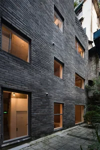 A modern building exterior constructed with dark grey bricks, featuring large windows and a courtyard.