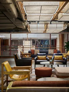 A modern hotel lobby featuring multiple seating areas with a mix of materials including leather, wood, and fabric.