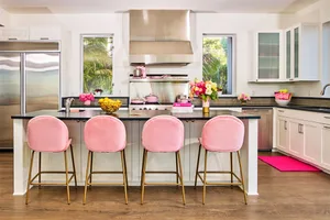 A modern kitchen with sleek metallic finishes and pink velvet cushioned stools.
