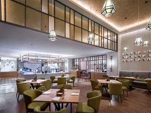 A modern restaurant interior with wooden furniture and glass walls, featuring contemporary lighting and seating arrangements.
