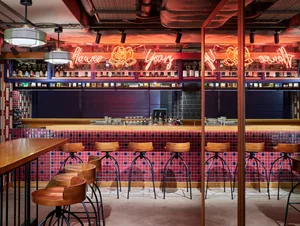 Modern restaurant interior with tile bar, wooden stools, and neon signage.