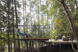 A person relaxing on a wooden platform with a metal railing in a forest setting.