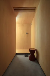 A minimalist entryway featuring wood walls, a dark red chair, and grey slippers.
