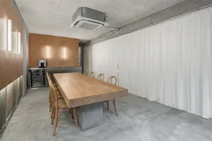 Industrial-style conference room with concrete flooring, wooden table and chairs, and minimalist design.