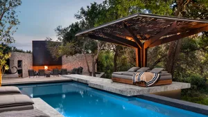 A modern residential pool side terrace featuring a fire pit, pergola, and seating area surrounded by natural stone and concre
