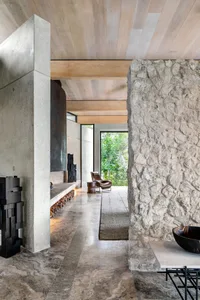 A modern living room featuring concrete walls, floor, and ceiling, with a cozy fireplace and a view of greenery outside.