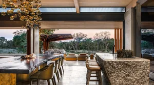A modern restaurant bar with wooden stools, concrete countertops, and a glass chandelier.