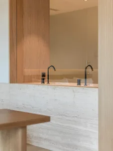 A minimalist bathroom with marble walls and black faucets.