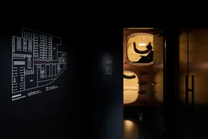 極簡臥室內，一人坐在膠囊旅館房間裡使用智慧型手機。