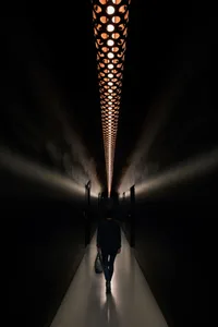 A minimalist corridor illuminated by a futuristic, perforated lighting fixture made of concrete.