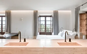 Modern bedroom featuring a marble stone floor and white bedding with a view of greenery through open double doors.