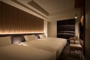A modern hotel bedroom with three cushioned beds, wooden headboards, and a large wooden panel wall with recessed lighting.