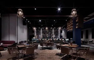 A modern restaurant bar with concrete walls and leather seating, featuring a well-lit central area with tables and chairs.