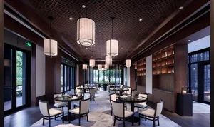 A modern restaurant interior with round tables, white chairs, large windows, and a decorative ceiling.