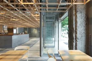 A minimalist coffee shop interior with wood tables, concrete walls, and glass doors.
