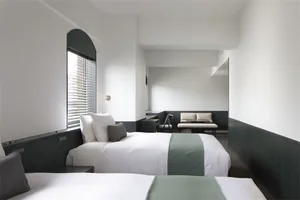 A minimalist hotel room with white walls and neutral-colored bedding, featuring a modern bench and minimalist decor.