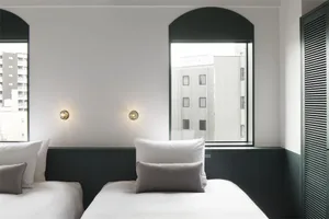 A minimalist hotel room with white walls and bedding.