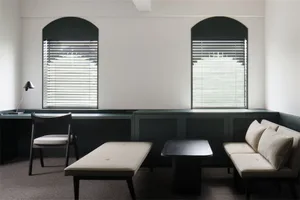 A minimalist interior space with neutral-toned furnishings and arch-shaped windows with blinds.