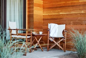 Two minimalist white folding chairs with wooden legs and arms placed outdoors on a wooden deck, with a white blanket draped o