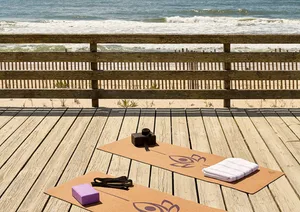 A minimalist yoga room with wooden flooring and mats on a beach overlooking the ocean.