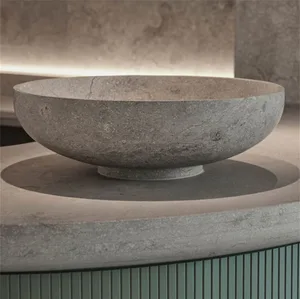 A minimalist, circular concrete bowl with a textured surface placed on a concrete surface.