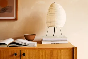 A modern interior design featuring a wooden cabinet, an open book, a ceramic bowl, and a paper lampshade.
