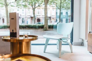 A modern restaurant interior featuring a polished cement floor with a sleek white chair and a menu on a brass table.